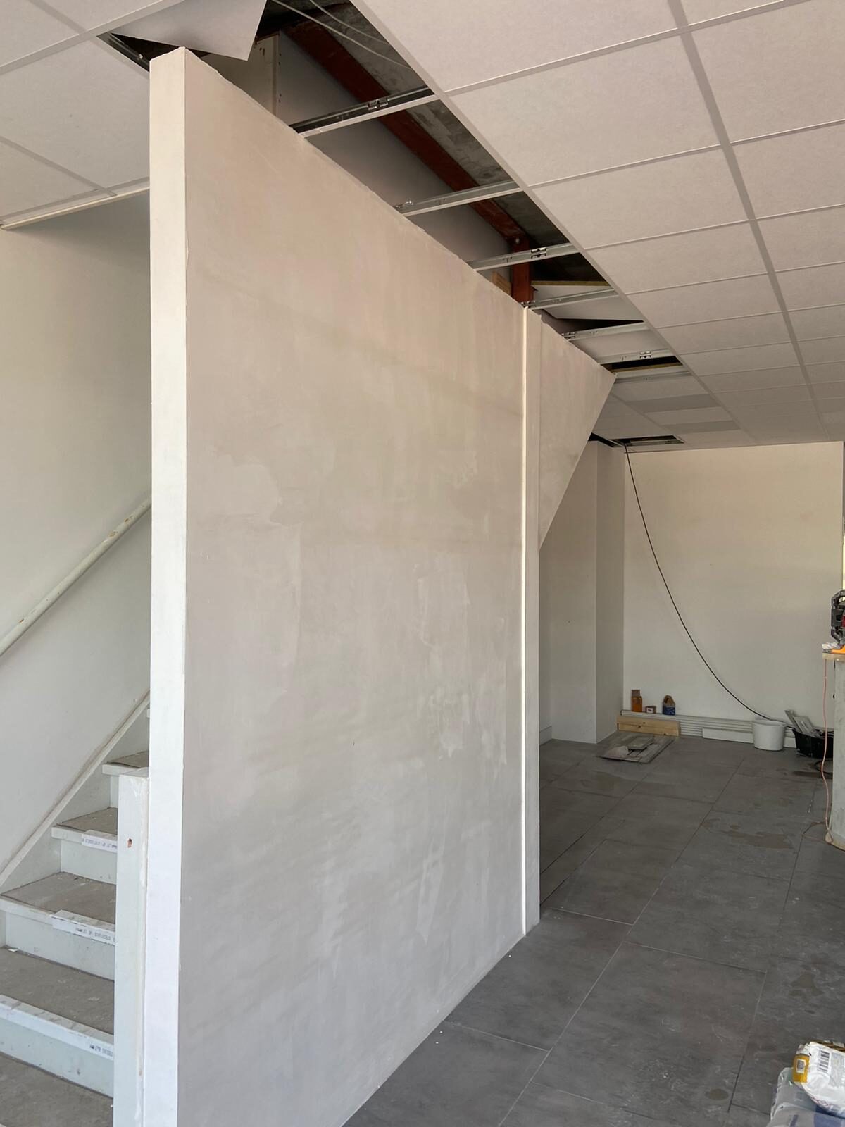 Opgebouwde gestukadoorde scheidingswand met zichtbaar staal-skelet boven verlaagd plafond