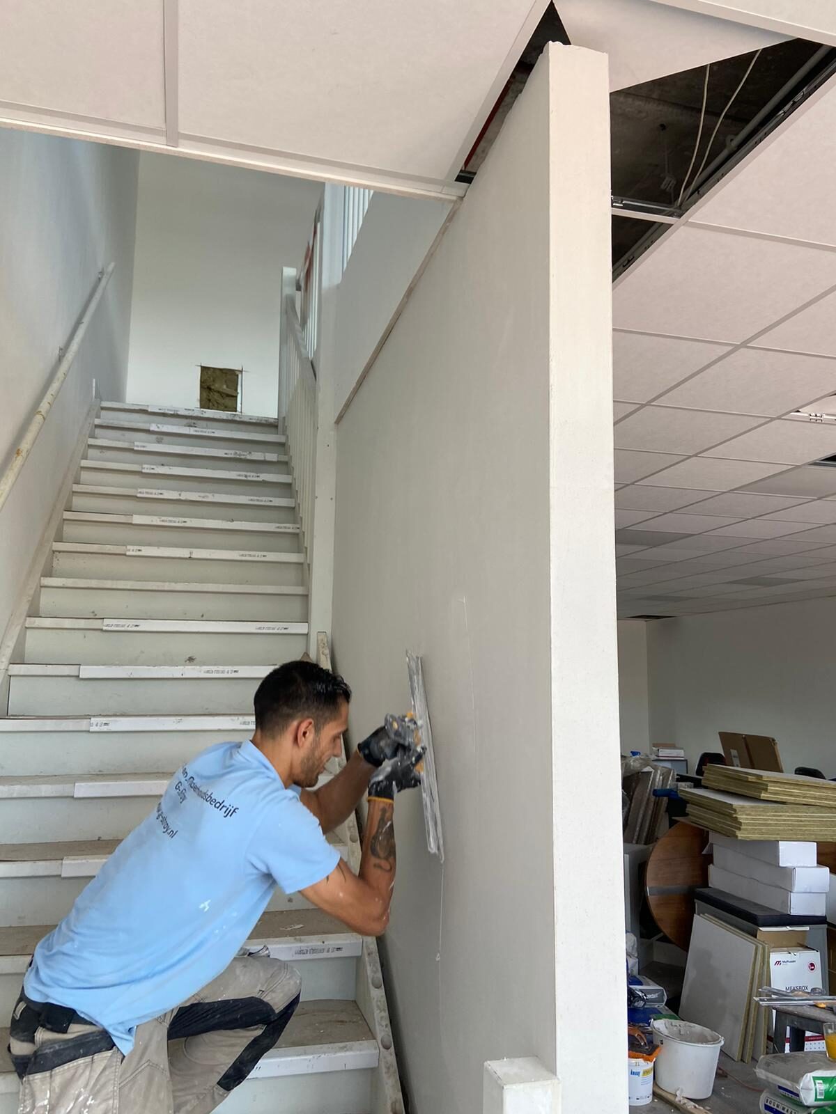 Stukadoor brengt gladde pleisterlaag aan op nieuwe scheidingswand naast trappenhuis tijdens casco fase
