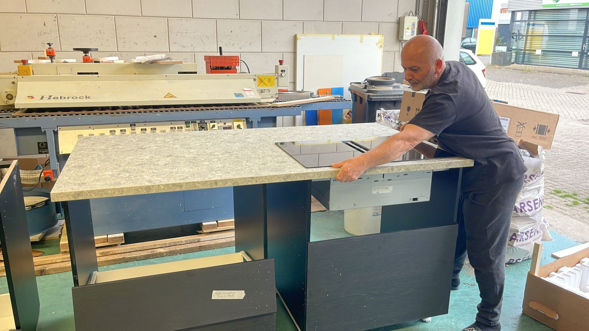 Productie van maatwerk keukenblad in het atelier — vakman past kookplaat in granieten werkblad
