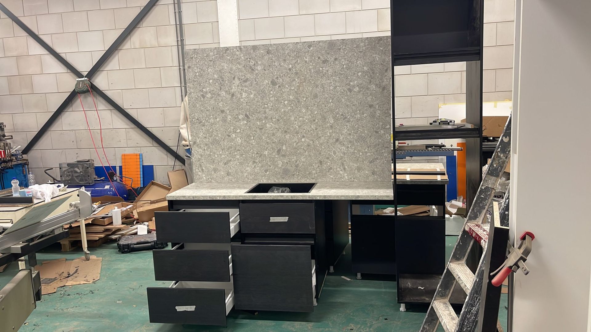Maatwerk keukeneiland in productie met granieten achterwand en donkere fronten