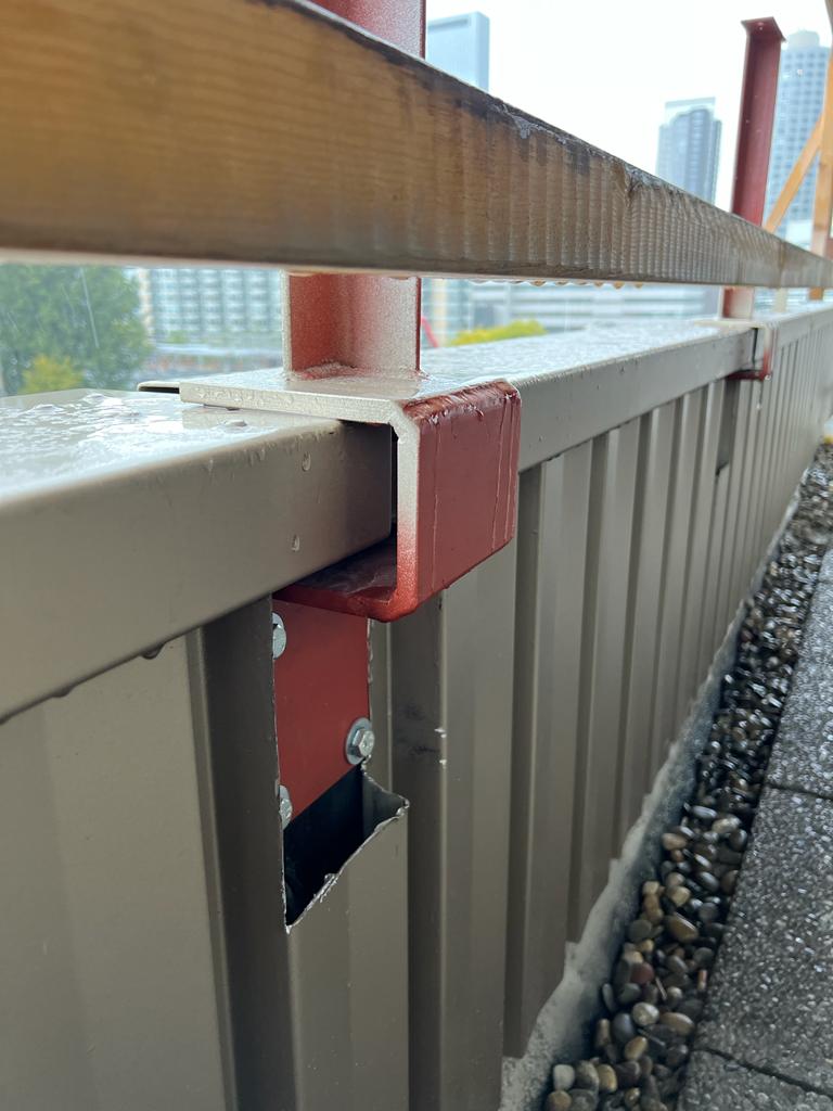 Detail — rode stalen U-beugel onder de houten dwarsligger