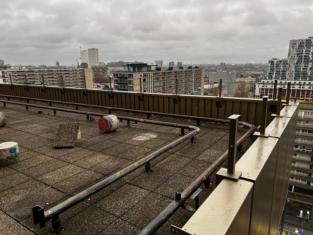 Rij stalen staanders langs de dakrand met skyline van Rotterdam