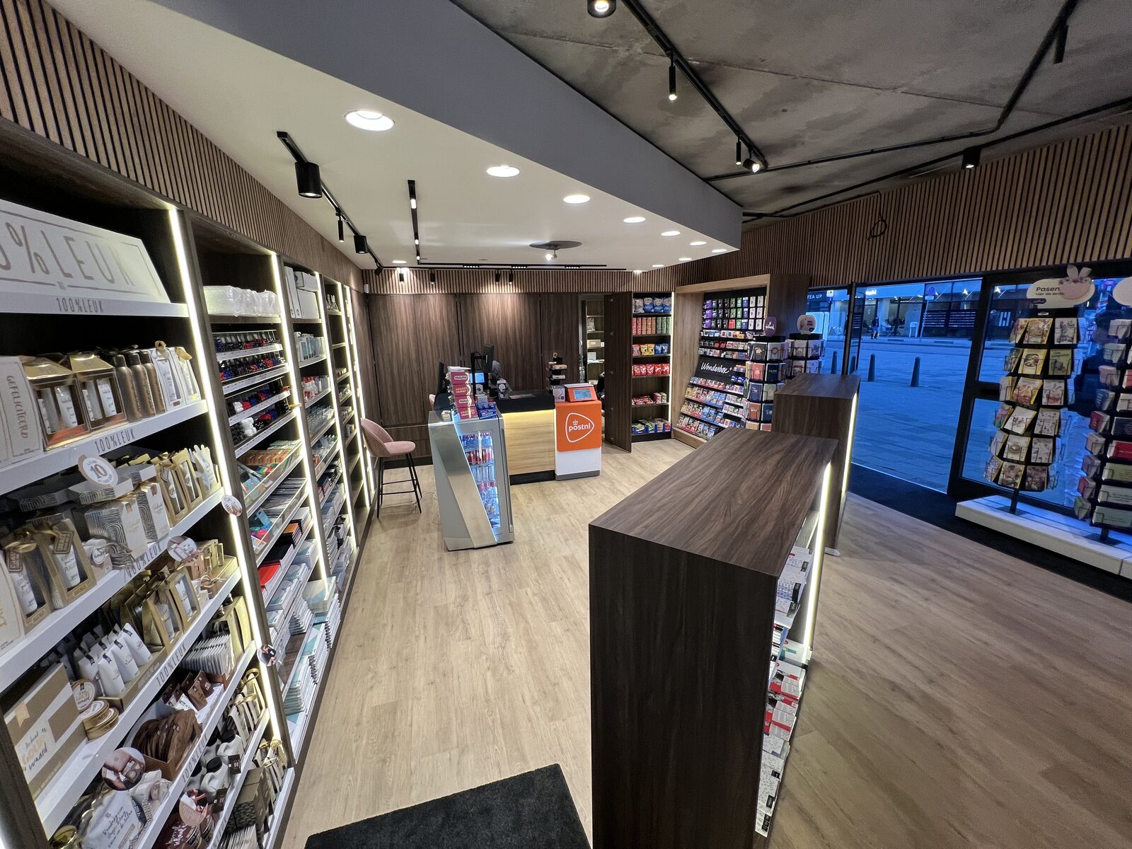Opgeleverde news & convenience store — overzicht winkelvloer met PostNL-balie en eikfineer displays
