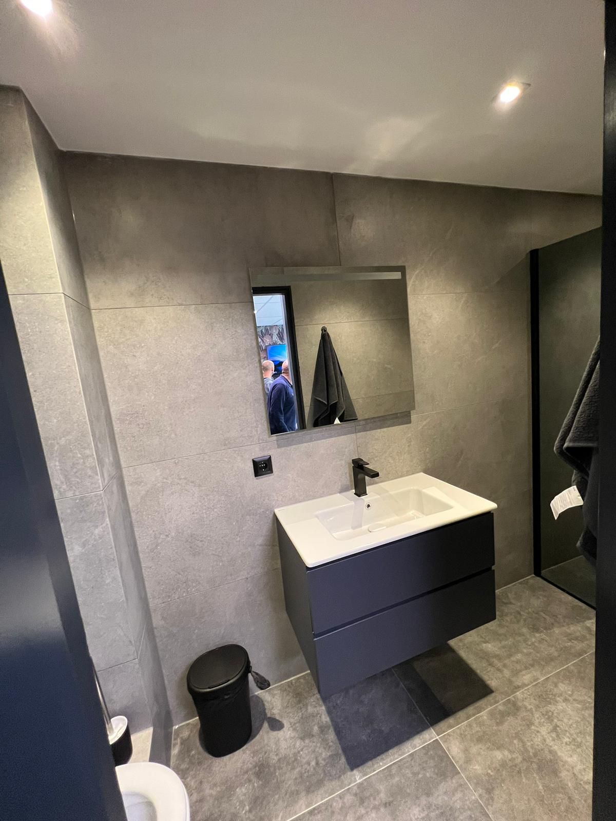 Wand­hangende vanity in donkerblauw met witte porseleinen wastafel, mat-zwarte kraan en spiegel